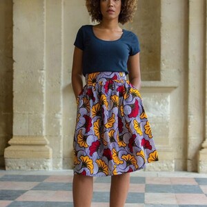 May include: A woman wearing a navy blue t-shirt and a high-waisted skirt with a colorful floral print. The skirt has a gathered waistband and pockets. She is wearing black heeled sandals.