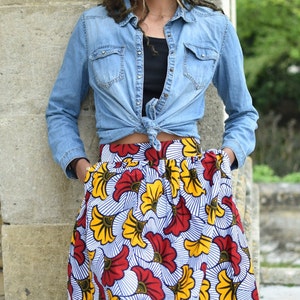 May include: A woman wearing a blue denim shirt tied at the waist over a black top and a colorful floral skirt with red, yellow, and white flowers.