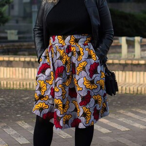 May include: A woman wearing a black leather jacket, a black turtleneck sweater, and a colorful floral skirt. She is wearing black tights and black shoes.