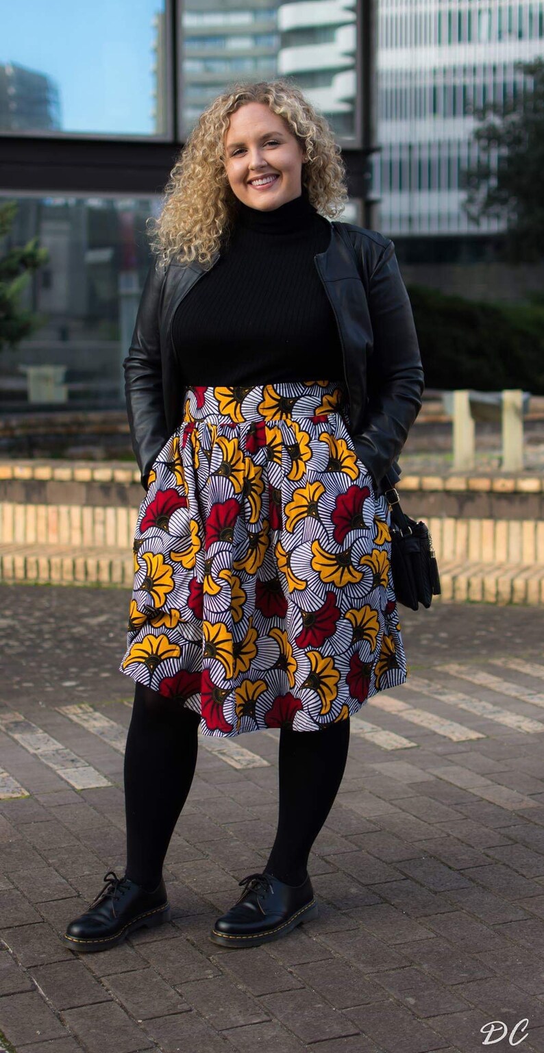 May include: A woman wearing a black leather jacket, a black turtleneck sweater, and a colorful floral skirt. She is wearing black tights and black shoes.