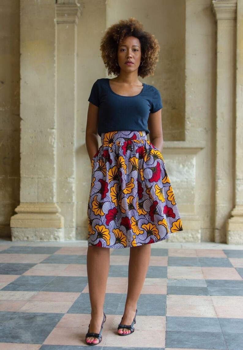 May include: A woman wearing a navy blue t-shirt and a high-waisted skirt with a colorful floral print. The skirt has a gathered waistband and pockets. She is wearing black heeled sandals.