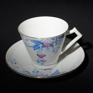 May include: A white teacup and saucer with a blue and pink floral pattern. The cup has a gold rim and the saucer has a gold band around the edge.