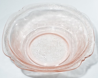 May include: A pink glass bowl with a delicate floral pattern. The bowl has a scalloped edge and a slightly raised center.