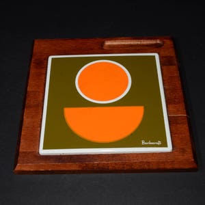 May include: A wooden serving tray with a ceramic tile insert featuring a geometric design of orange and green circles. The tile is labeled "Burkencraft".