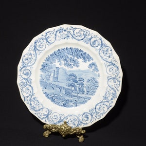 May include: A white ceramic plate with a blue and white floral design. The plate features a blue and white landscape scene with a bridge and trees.
