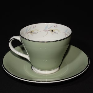 Puede incluir: Un juego de taza y platillo de té verde con un diseño floral. La taza y el platillo tienen un borde dorado.