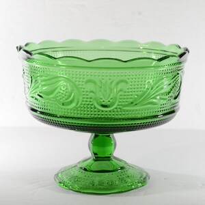 May include: A green glass pedestal bowl with a scalloped rim and a decorative floral pattern. The bowl is on a white background.