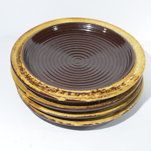 May include: A stack of four brown ceramic plates with a yellow rim. The plates have a spiral design.