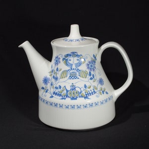May include: White teapot with a blue and green floral design featuring a girl holding a teapot. The teapot has a lid and a handle.