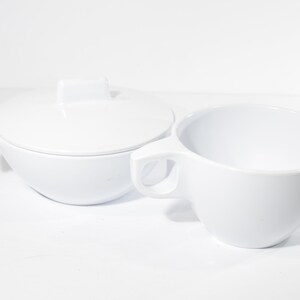 May include: White ceramic sugar bowl and creamer set. The sugar bowl has a lid with a square handle. The creamer has a handle and a spout.