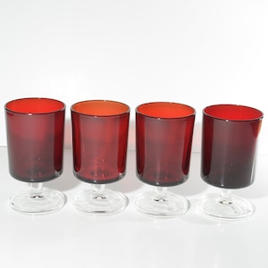 May include: Set of four red glass stemmed drinking glasses. The glasses are clear with a red tint and have a short stem.