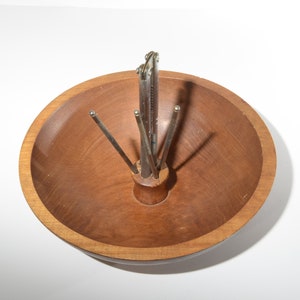 Pode incluir: Um quebra-nozes de madeira com um mecanismo de quebra-nozes de metal no centro de uma tigela de madeira. O quebra-nozes tem cinco pontas que se estendem do centro.