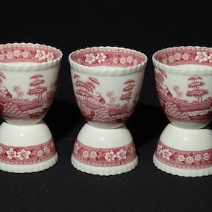 May include: Three white ceramic egg cups with a pink floral pattern. The cups are stacked on top of each other.