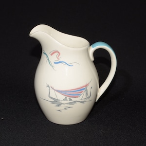 May include: A white ceramic creamer with a blue handle and a nautical scene painted on the side. The scene features a boat with a striped sail and blue and red ribbons.