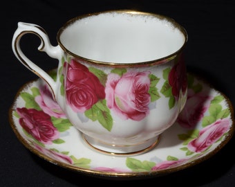 May include: A white teacup and saucer with a floral pattern of pink and red roses. The cup and saucer have a gold trim.