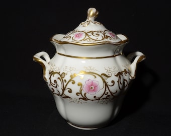 Könnte beinhalten: Weiße Porzellan-Zuckerdose mit Deckel, verziert mit rosa Blumen und goldenen Ranken.