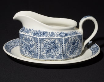 May include: A white ceramic gravy boat with a blue floral pattern and a matching saucer. The boat has a rounded spout and a handle.