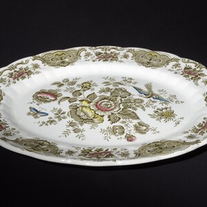 Könnte beinhalten: Ovale Servierplatte mit weißem Grund und floralem Design mit rosa, gelben und grünen Blumen sowie blauen Vögeln. Der Rand hat eine dekorative Bordüre in Grün- und Goldtönen.