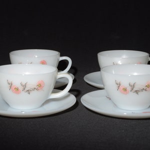 May include: Set of four white teacups and saucers with a floral design. The cups and saucers have a delicate pink and gray floral pattern.