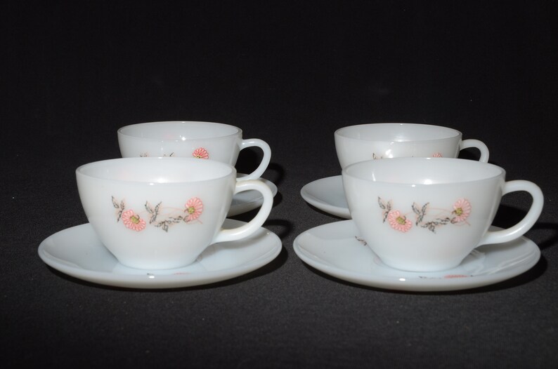 May include: Set of four white teacups and saucers with a floral design. The cups and saucers have a delicate pink and gray floral pattern.