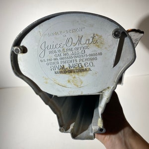 May include: A vintage silver-colored "Juice-O-Mat" single-action juicer with the text "REG. U.S. PAT. OFFICE CAT. NO. 462-CJ U.S. PAT-NO. DI05335-2142975-D118840 OTHER PATENTS PENDING RIVAL MEG. CO. KANSAS CITY, MO. U.S.A."