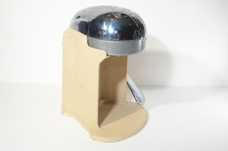 May include: A chrome and beige manual citrus juicer with a lever on the side. The juicer is made of metal and has a beige plastic base.