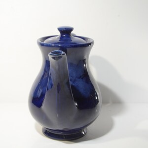 May include: A cobalt blue ceramic teapot with a rounded body and a lid. The teapot has a spout and a handle.