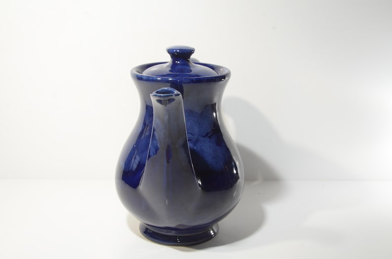 May include: A cobalt blue ceramic teapot with a rounded body and a lid. The teapot has a spout and a handle.