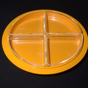 Może przedstawiać: Okrągłe, pomarańczowe naczynie do serwowania z czterema przezroczystymi, podzielonymi sekcjami. Naczynie jest wykonane z tworzywa sztucznego i ma gładkie, błyszczące wykończenie.