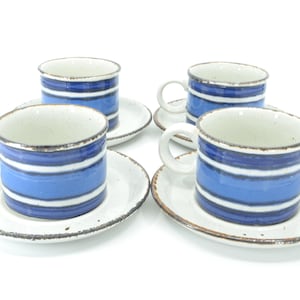 Könnte beinhalten: Set aus vier Keramik-Kaffeetassen und Untertassen. Die Tassen haben blaue und weiße horizontale Streifen und weiße Griffe. Die Untertassen sind weiß mit braunem Rand. Ein klassisches Design.