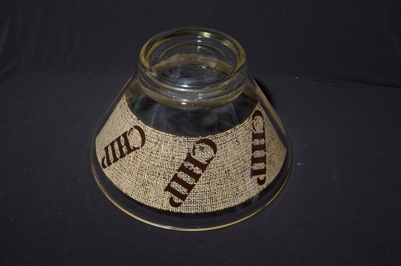 Puede incluir: Un bol de vidrio transparente para chips y salsa con una textura de arpillera y la palabra "Chip" impresa en marr&oacute;n en los lados.