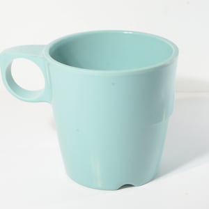Może przedstawiać: Jasnoniebieski kubek ceramiczny z uchwytem. Kubek jest pusty i ma gładką, zaokrągloną powierzchnię.