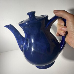 May include: A cobalt blue ceramic teapot with a rounded body and a spout. The teapot has a lid with a knob on top.