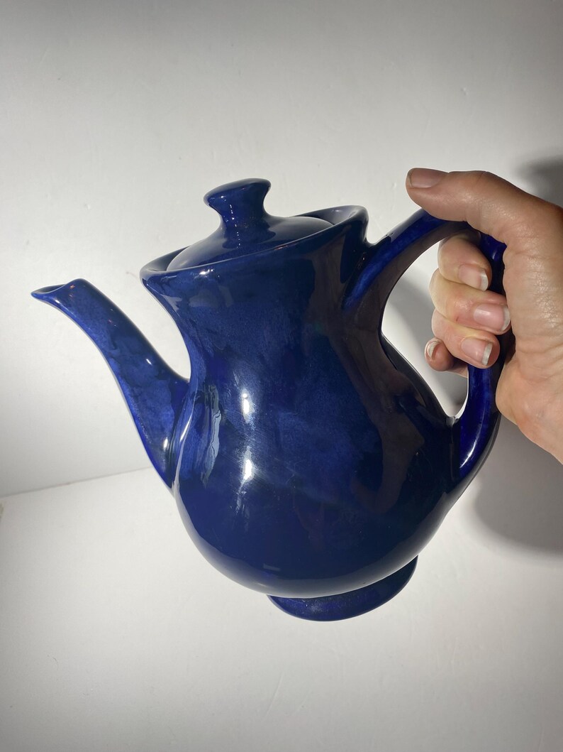 May include: A cobalt blue ceramic teapot with a rounded body and a spout. The teapot has a lid with a knob on top.