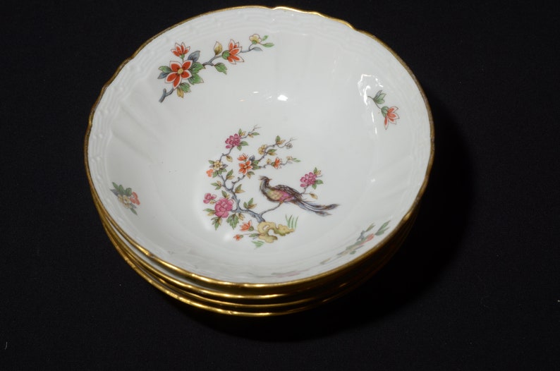 May include: A set of four white porcelain bowls with gold trim and a floral design featuring a bird. The bowls are stacked on top of each other.