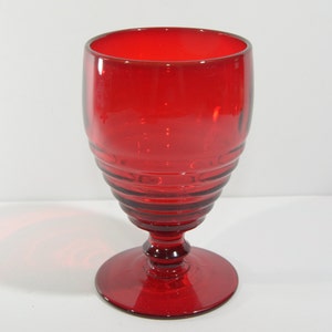 Könnte beinhalten: Ein rotes Glasgefäß mit geriffeltem Design und einem Stiel.