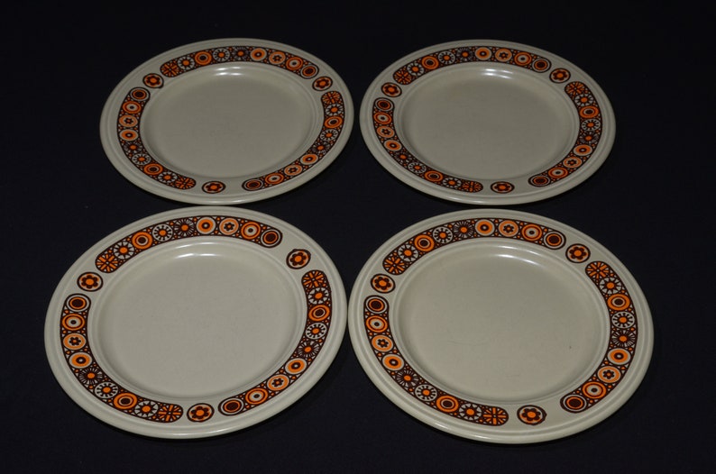 May include: Set of four beige ceramic plates with a brown and orange geometric pattern around the rim.
