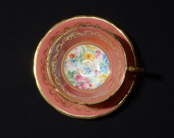May include: A pink teacup and saucer with a floral pattern and gold trim. The cup and saucer are decorated with a delicate floral design in shades of pink, yellow, and blue.
