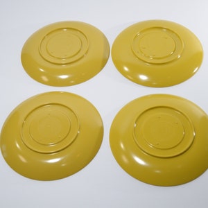 May include: Four yellow ceramic plates with a raised center circle. The plates are all the same size and shape.