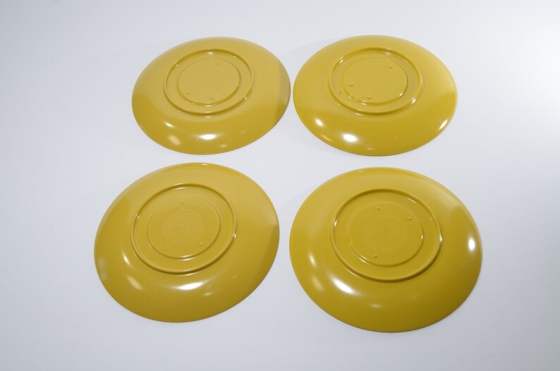 May include: Four yellow ceramic plates with a raised center circle. The plates are all the same size and shape.