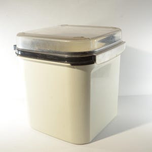 Könnte beinhalten: Ein weißer Plastikbehälter mit einem durchsichtigen Plastikdeckel. Der Behälter hat eine schwarze Gummidichtung um den Deckel.