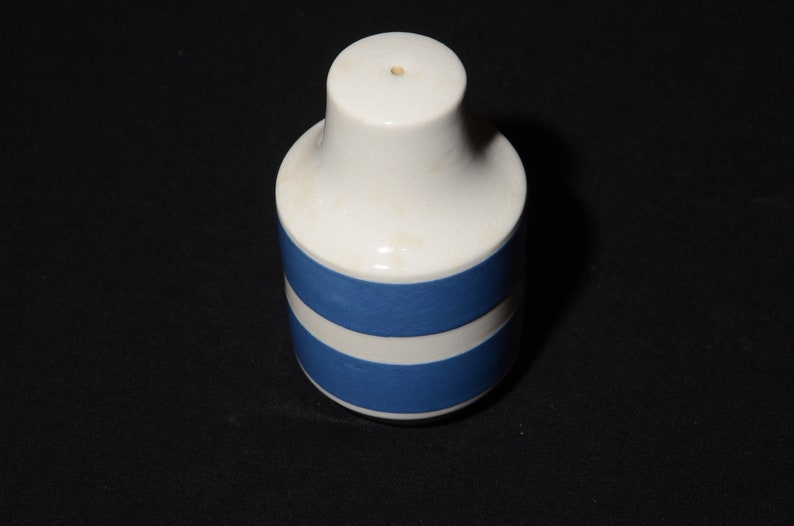May include: A white ceramic salt shaker with two blue stripes around the middle.