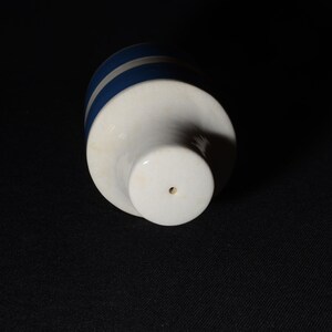 May include: White ceramic bottle stopper with a blue stripe design. The stopper has a small hole in the bottom.