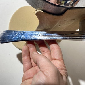 May include: A chrome car door handle with a textured surface. The handle is attached to a beige base.