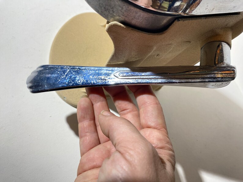 May include: A chrome car door handle with a textured surface. The handle is attached to a beige base.