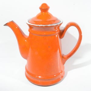 May include: Orange ceramic teapot with a white lid and a white rim around the top. The teapot has a rounded body and a spout on one side and a handle on the other.