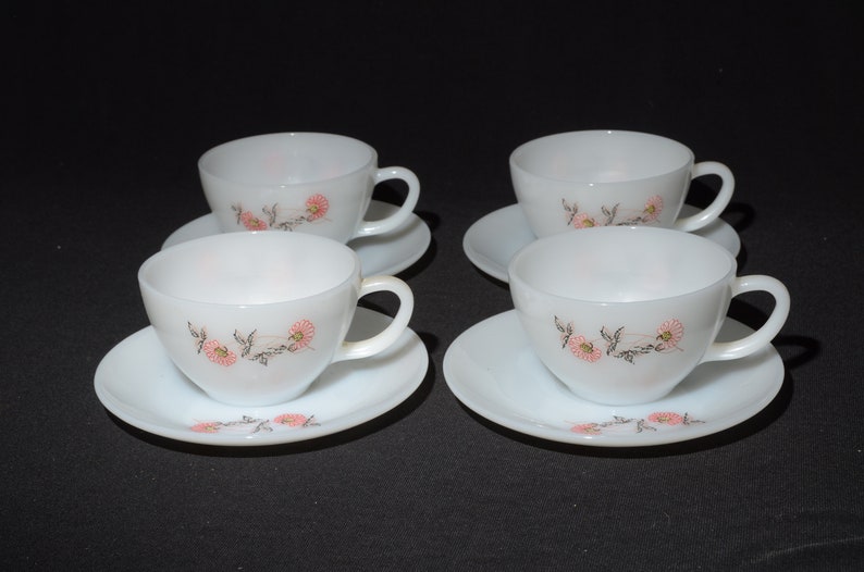 May include: Set of four white ceramic teacups and saucers with a floral design. The cups and saucers have a delicate pink and black floral pattern.
