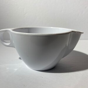 May include: A white plastic mixing bowl with a handle and a spout. The bowl is designed for pouring liquids.