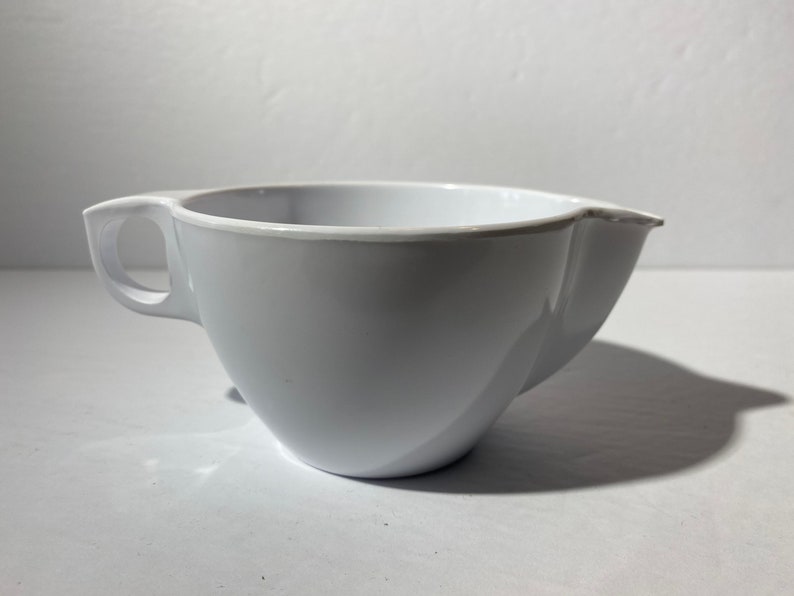 May include: A white plastic mixing bowl with a handle and a spout. The bowl is designed for pouring liquids.