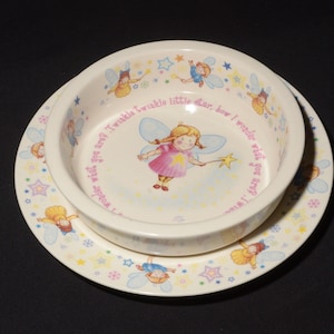 Puede incluir: Un juego de cuenco y plato de cerámica blanca para niños con un diseño de hada y estrella. El cuenco tiene el texto "Twinkle twinkle little star, how I wonder what you are? I wonder what you are?" El plato tiene un patrón repetitivo de hadas y estrellas.